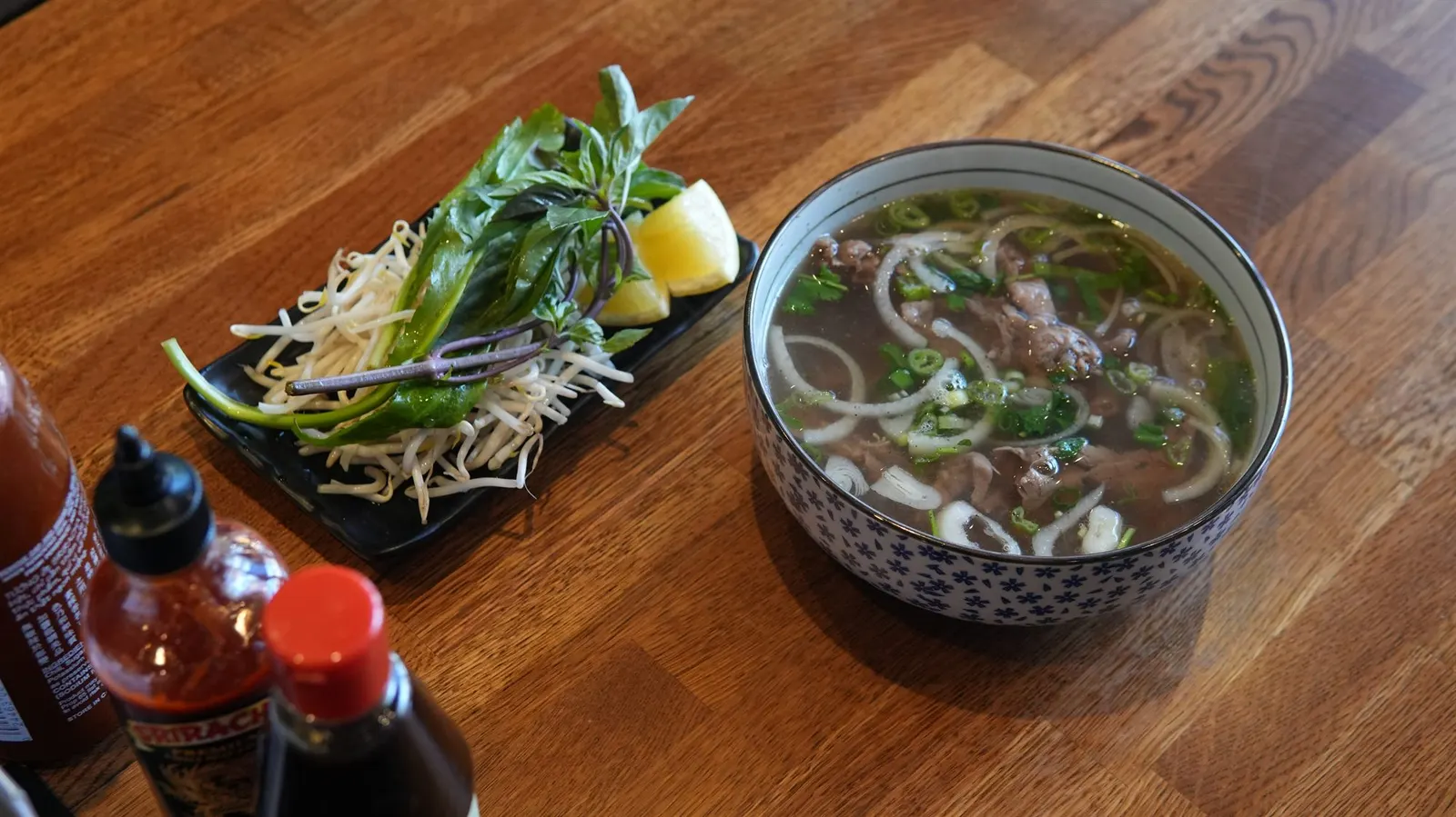 Fire Pho beef pho bowl with fresh garnishes and sriracha, served at 7451 Edinger Ave, Huntington Beach, CA.