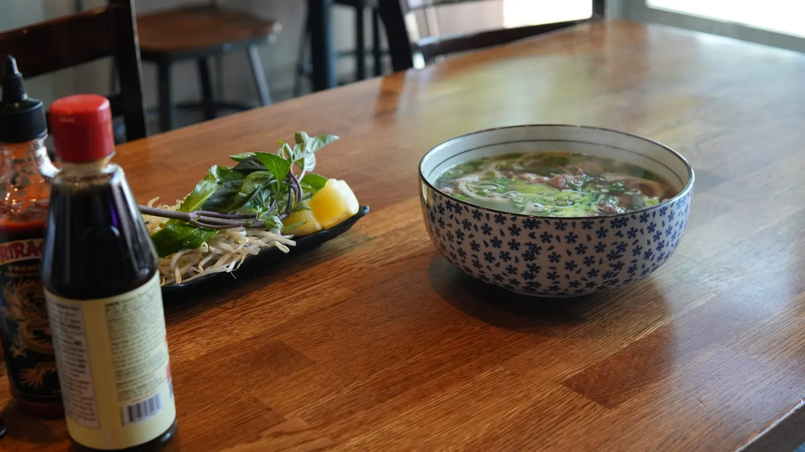 Vietnamese beef noodle soup with fresh herbs and sriracha on the table at Fire Pho in Huntington Beach, CA.