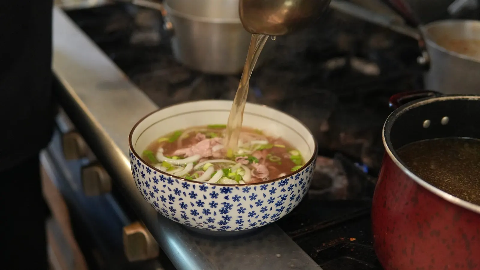 Chef pouring hot bone broth into a pho bowl at Fire Pho in Huntington Beach, CA.
