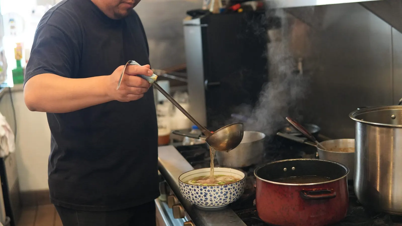 Fire Pho chef ladling steaming 22-hour bone broth into a pho bowl in the kitchen at 7451 Edinger Ave, Huntington Beach, CA.