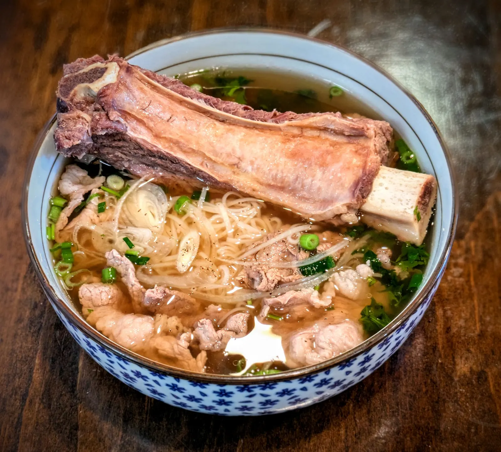 Bowl of beef pho with rare steak, rice noodles, and fresh herbs at Fire Pho, Edinger Ave, Huntington Beach, CA.